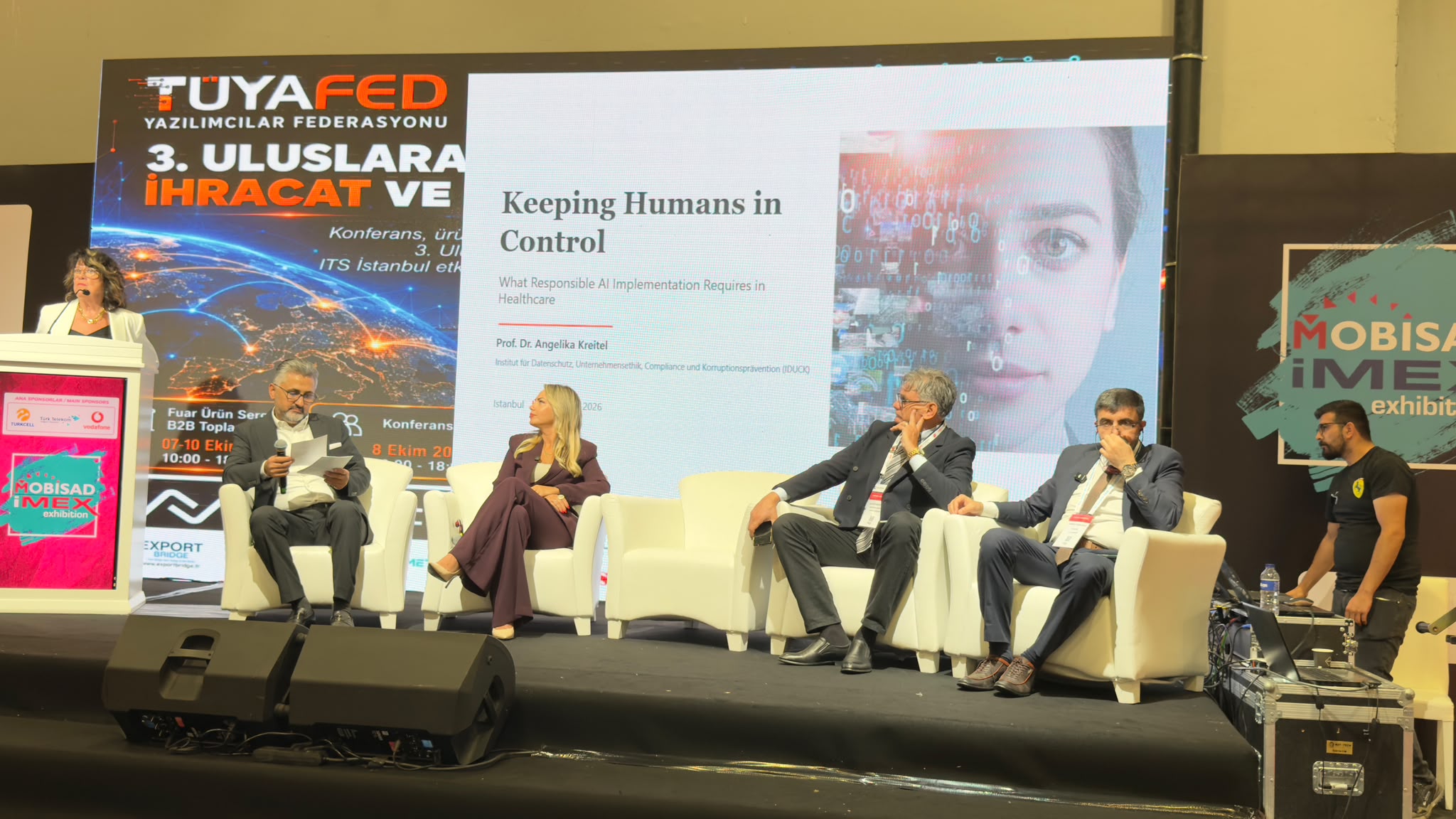 Prof. Dr. Angelika Kreitel am Rednerpult; auf der Bühne ist die Titelfolie Keeping Humans in Control zu sehen